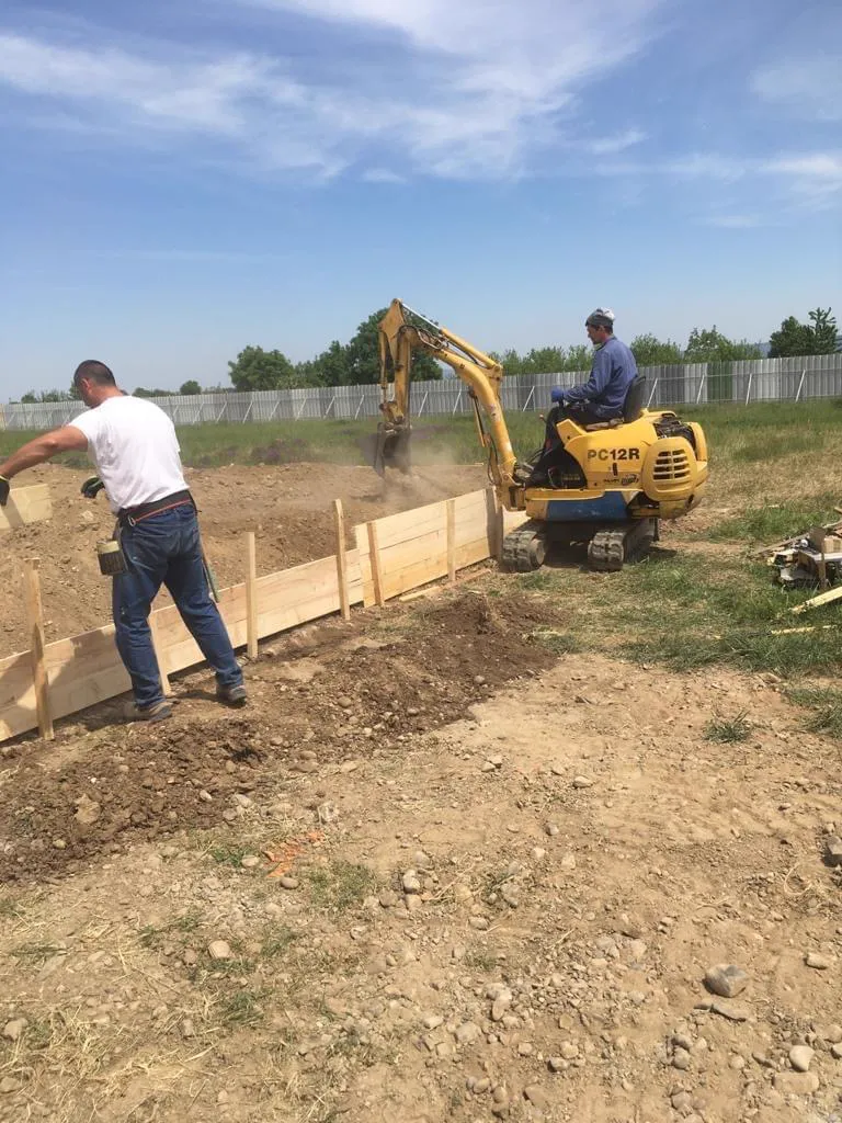 A small excavator preparing the ground beside the formwork.