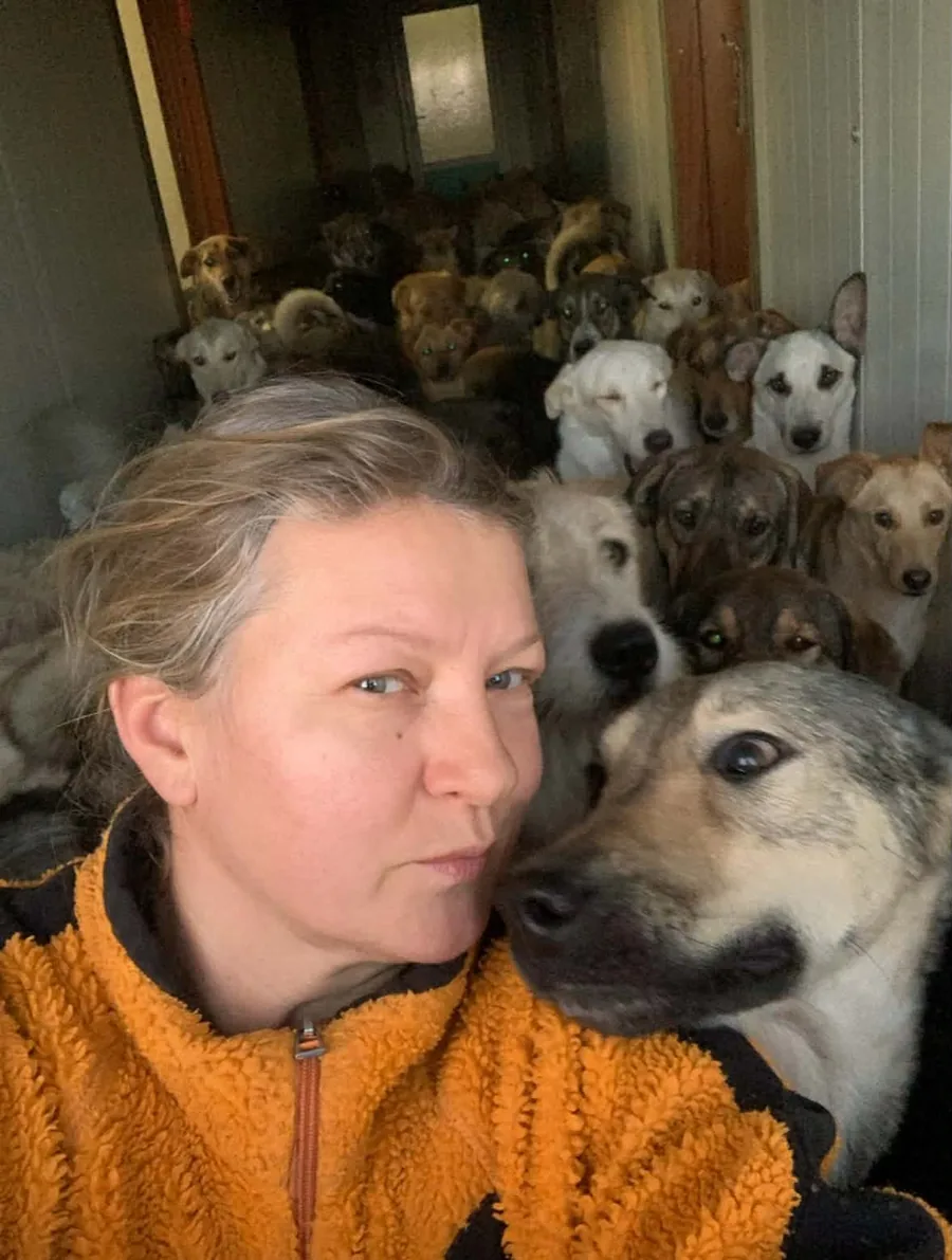 Mirela in an orange fleece, a dog leaning its head against her cheek, the whole pack crowding the corridor behind them.
