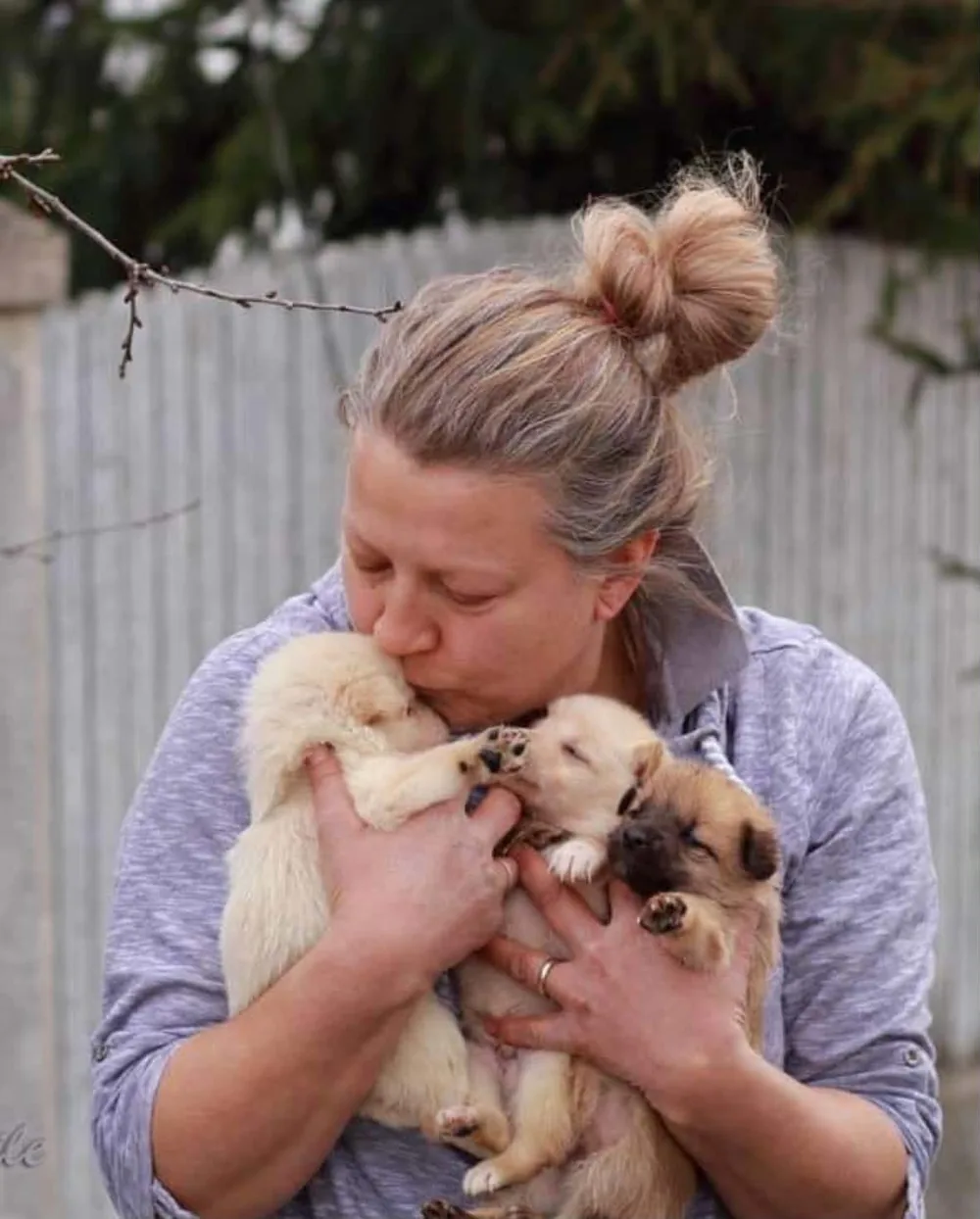 Mirela kissing three sleeping puppies she holds against her chest.
